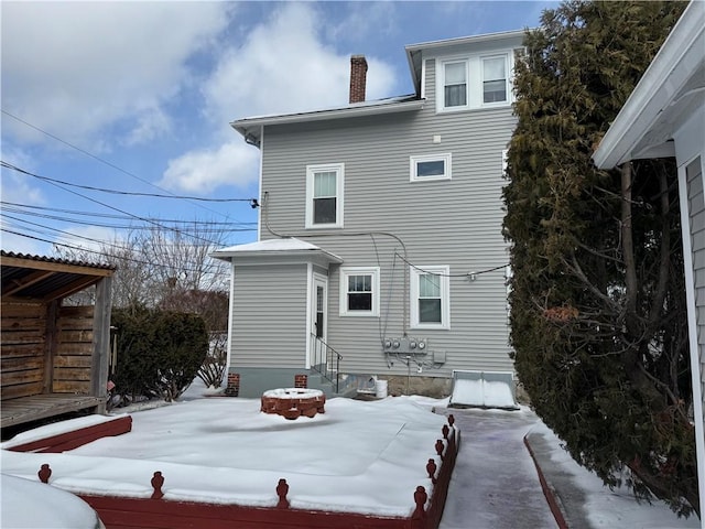 snow covered rear of property with entry steps and a chimney