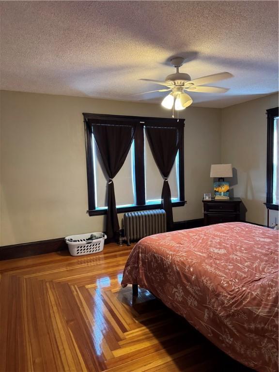 bedroom with radiator heating unit, a ceiling fan, a textured ceiling, and wood finished floors