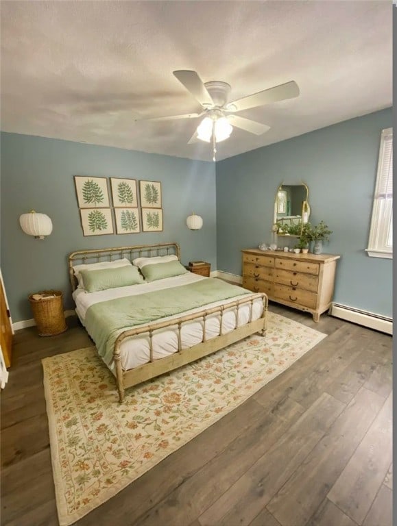 bedroom with ceiling fan, baseboard heating, and dark wood-type flooring