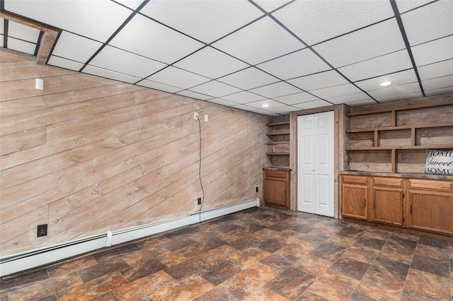 interior space with a paneled ceiling, wooden walls, and a baseboard heating unit