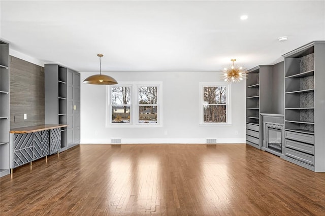 unfurnished living room with a fireplace, built in shelves, a chandelier, and dark hardwood / wood-style flooring