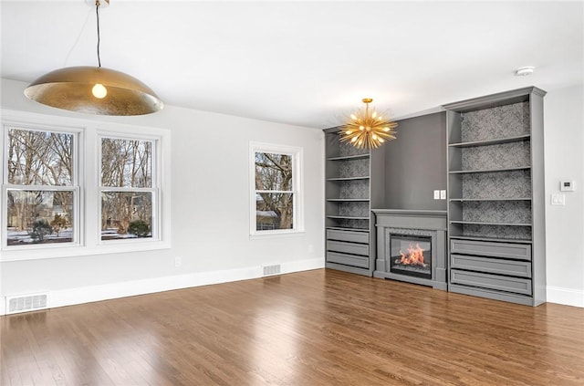 unfurnished living room featuring a chandelier, dark hardwood / wood-style flooring, and built in shelves