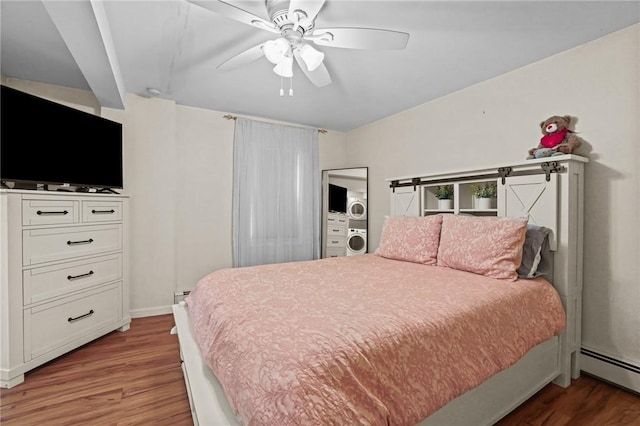 bedroom with baseboard heating, ceiling fan, wood-type flooring, and stacked washer and clothes dryer