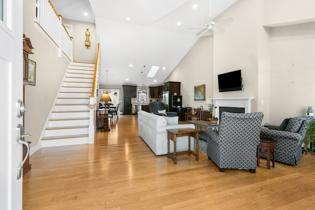 living room featuring light wood finished floors, stairway, a fireplace, high vaulted ceiling, and recessed lighting