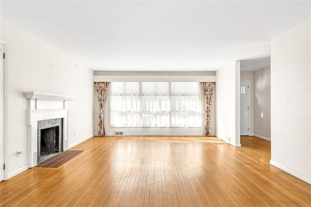 unfurnished living room with wood-type flooring, visible vents, a fireplace, and baseboards