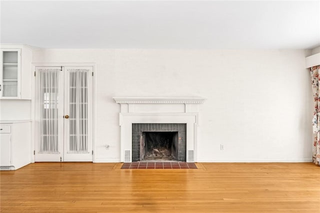 unfurnished living room with light wood-type flooring, a brick fireplace, and baseboards