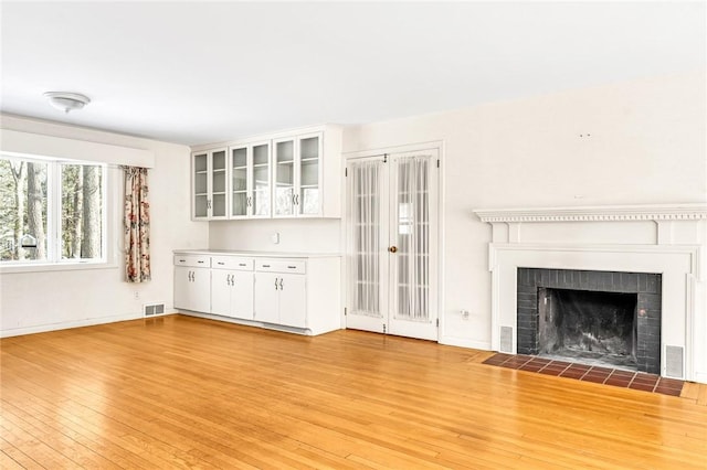 unfurnished living room with light wood-style floors, visible vents, a fireplace, and baseboards