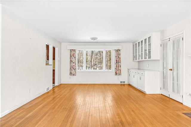 unfurnished living room with light wood-style flooring, visible vents, and baseboards