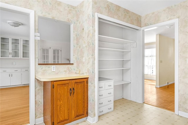 interior space with wallpapered walls, baseboards, brown cabinetry, light countertops, and light floors