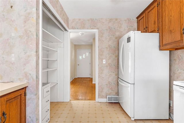 kitchen featuring visible vents, brown cabinetry, freestanding refrigerator, and wallpapered walls