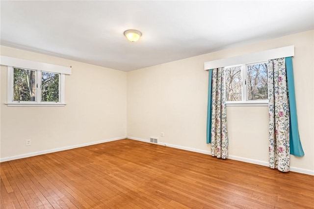 spare room featuring light wood-type flooring, visible vents, and baseboards