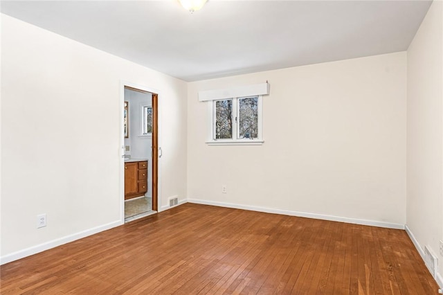 spare room featuring hardwood / wood-style floors, visible vents, and baseboards