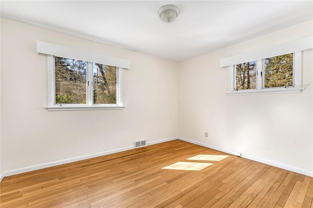 unfurnished room with light wood-type flooring, visible vents, and baseboards