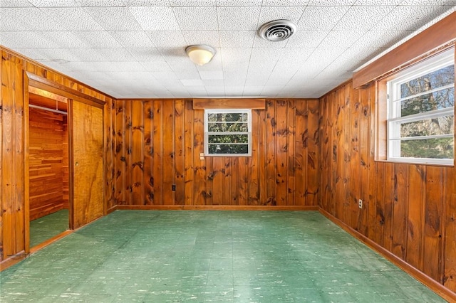 spare room with wood walls, visible vents, and a healthy amount of sunlight