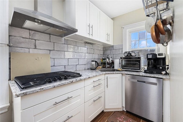 kitchen with stainless steel appliances, white cabinets, a sink, and wall chimney range hood