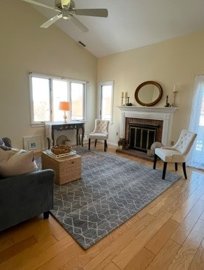 living area with visible vents, ceiling fan, wood finished floors, a brick fireplace, and high vaulted ceiling