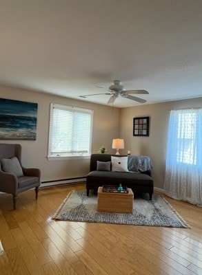 living room with a baseboard heating unit, light wood finished floors, and a ceiling fan