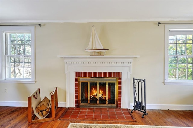 details with ornamental molding, a brick fireplace, wood finished floors, and baseboards