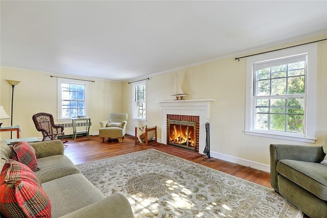 living room with a brick fireplace, baseboards, wood finished floors, and ornamental molding