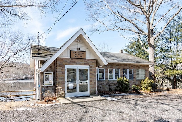 view of front of home with stone siding, a chimney, fence, and roof with shingles