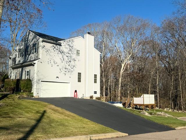 view of home's exterior featuring stucco siding, a lawn, driveway, a garage, and a chimney