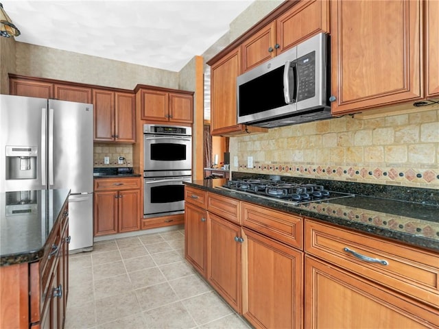 kitchen featuring brown cabinets, dark stone countertops, tasteful backsplash, appliances with stainless steel finishes, and light tile patterned flooring