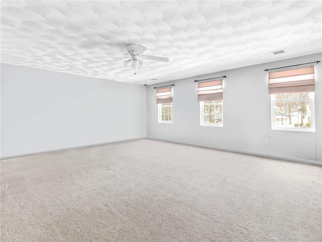 unfurnished room featuring a textured ceiling, carpet, visible vents, and ceiling fan