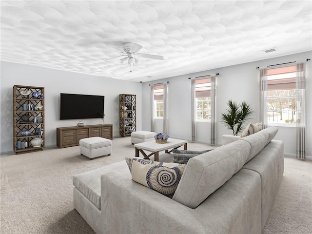 living area featuring visible vents, a ceiling fan, and light colored carpet