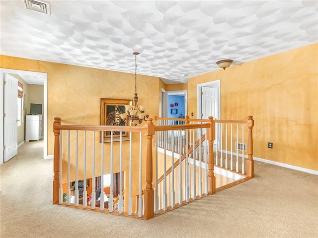 hallway featuring carpet flooring, a notable chandelier, an upstairs landing, and visible vents