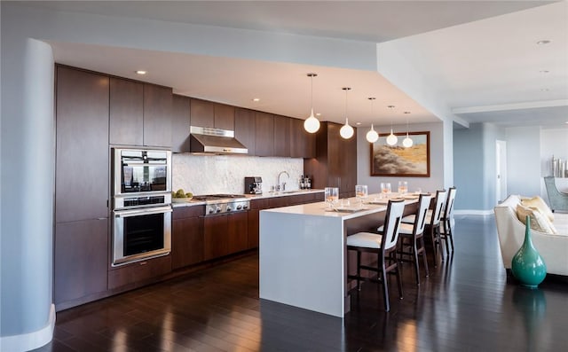 kitchen featuring a kitchen island, appliances with stainless steel finishes, light countertops, dark brown cabinets, and under cabinet range hood