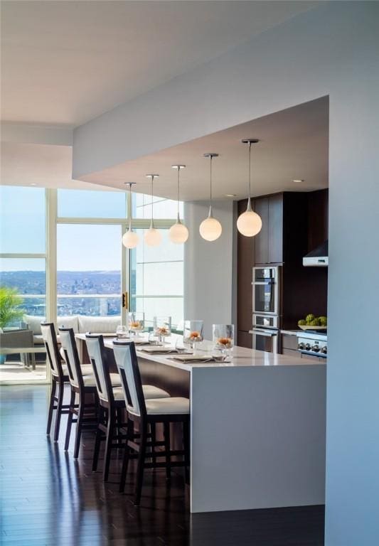 kitchen with stainless steel double oven, under cabinet range hood, light countertops, modern cabinets, and a kitchen bar