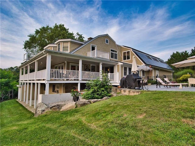 rear view of property with a patio area, a lawn, a balcony, and a gambrel roof