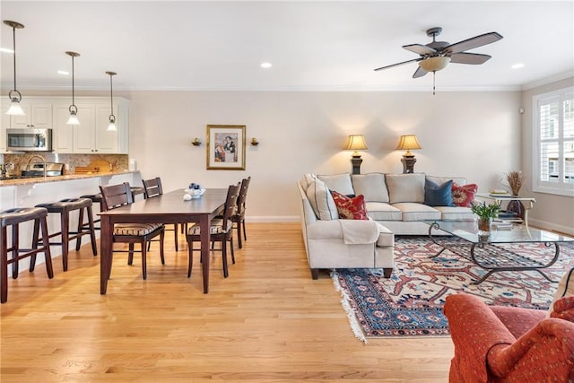 living room featuring baseboards, light wood-style flooring, ceiling fan, crown molding, and recessed lighting