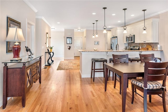 dining room with light wood finished floors, baseboards, ornamental molding, and recessed lighting