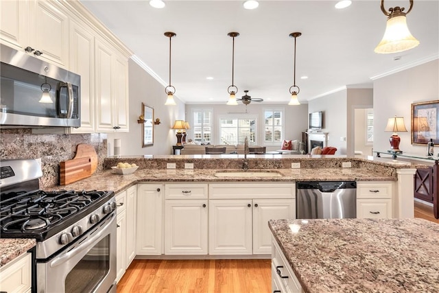 kitchen with appliances with stainless steel finishes, open floor plan, pendant lighting, and a sink