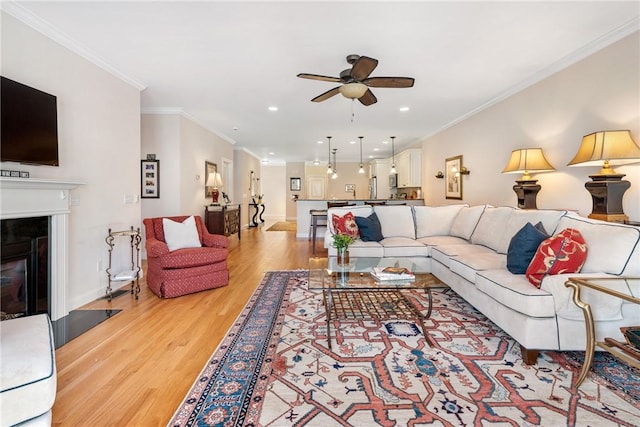 living room featuring light wood-style flooring, ornamental molding, a ceiling fan, and a glass covered fireplace