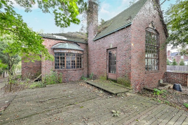 rear view of property with brick siding, a chimney, and a wooden deck