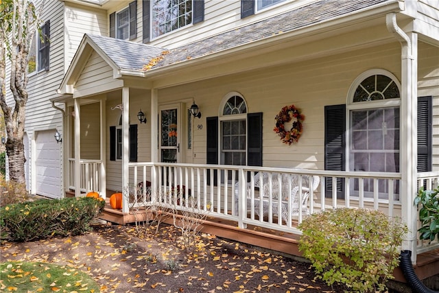 entrance to property featuring an attached garage, covered porch, and roof with shingles