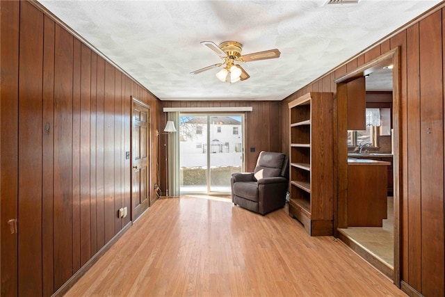 unfurnished room featuring light wood-type flooring, ceiling fan, and wooden walls