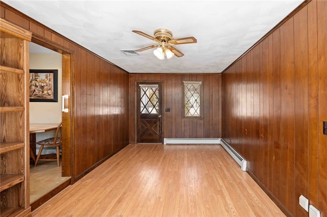 foyer entrance with light wood finished floors, wooden walls, visible vents, a ceiling fan, and a baseboard radiator