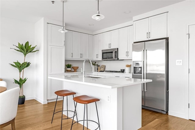 kitchen featuring pendant lighting, light countertops, appliances with stainless steel finishes, a kitchen island with sink, and white cabinetry