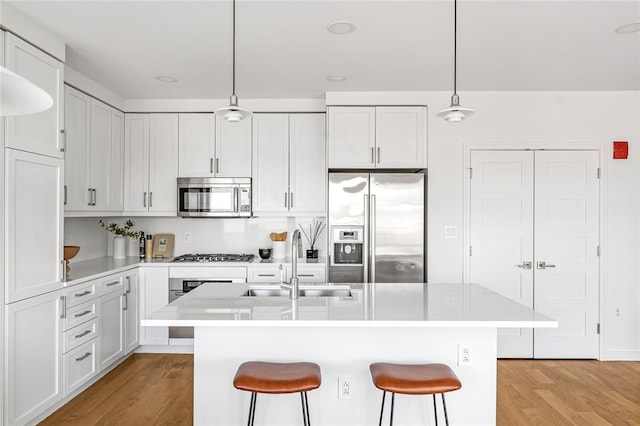 kitchen with pendant lighting, stainless steel appliances, light countertops, a kitchen island with sink, and a sink