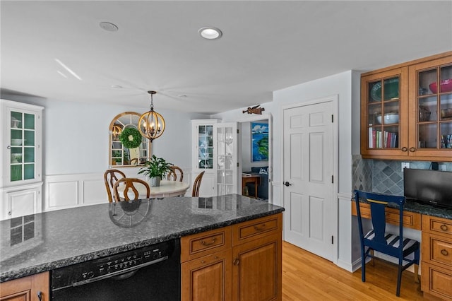 kitchen with light wood-style flooring, built in study area, dishwasher, brown cabinetry, and decorative light fixtures