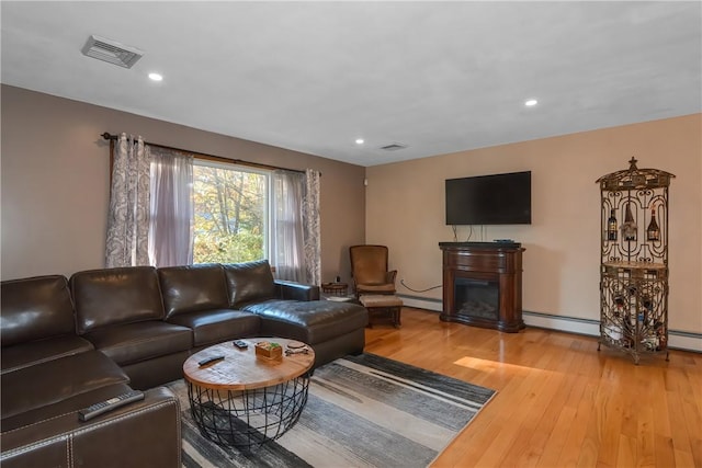 living room featuring a baseboard radiator, recessed lighting, wood finished floors, visible vents, and a glass covered fireplace