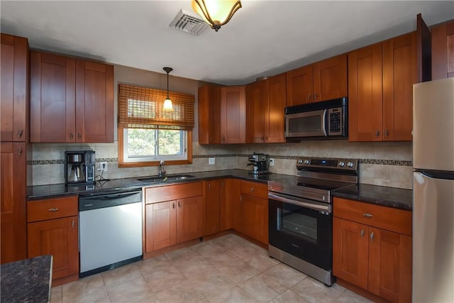 kitchen with stainless steel appliances, dark countertops, brown cabinetry, and a sink