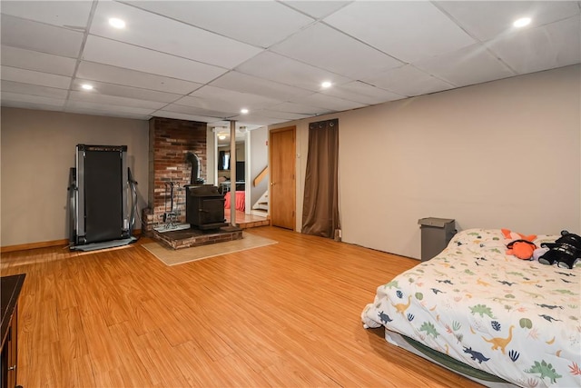 unfurnished bedroom featuring a drop ceiling, wood finished floors, and a wood stove