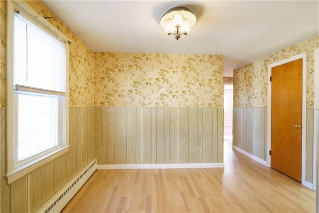 empty room with wainscoting, a baseboard radiator, light wood-style flooring, and wallpapered walls