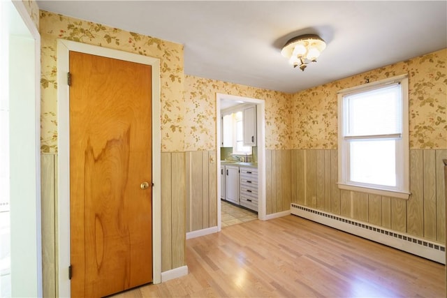 empty room with a baseboard radiator, a wainscoted wall, light wood finished floors, and wallpapered walls