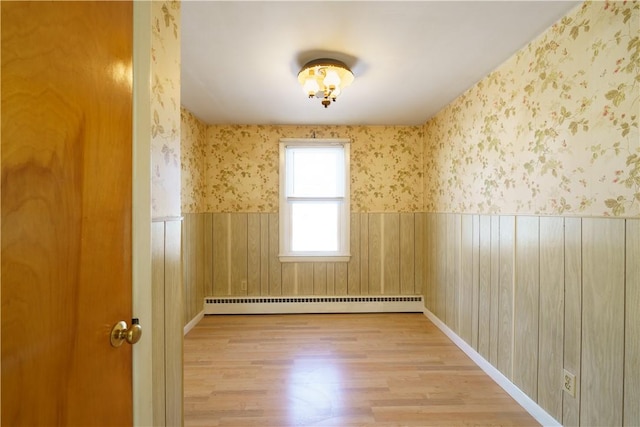 unfurnished room with light wood-type flooring, a wainscoted wall, baseboard heating, and wallpapered walls