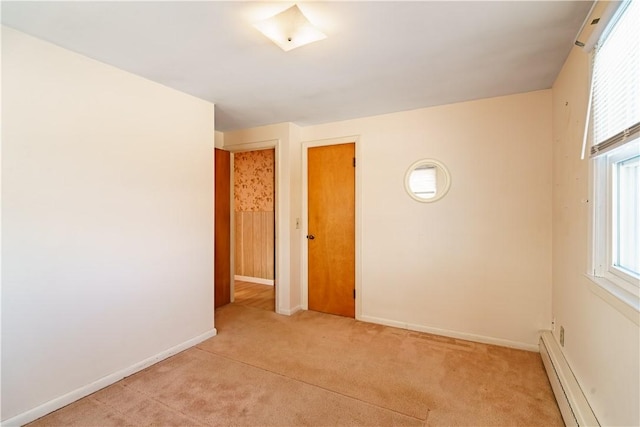 empty room with a baseboard radiator, light colored carpet, and baseboards